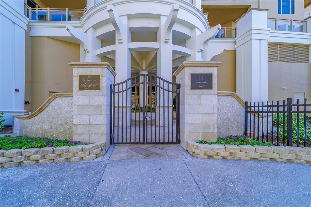 A gated entrance with stone pillars leads to a building exterior with architectural columns — 11 BAYMONT STREET UNIT 1109, CLEARWATER BEACH, FL