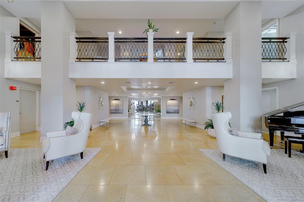 A spacious lobby features a two-story ceiling, tiled floors, white armchairs, and a grand piano — 11 BAYMONT STREET UNIT 1109, CLEARWATER BEACH, FL