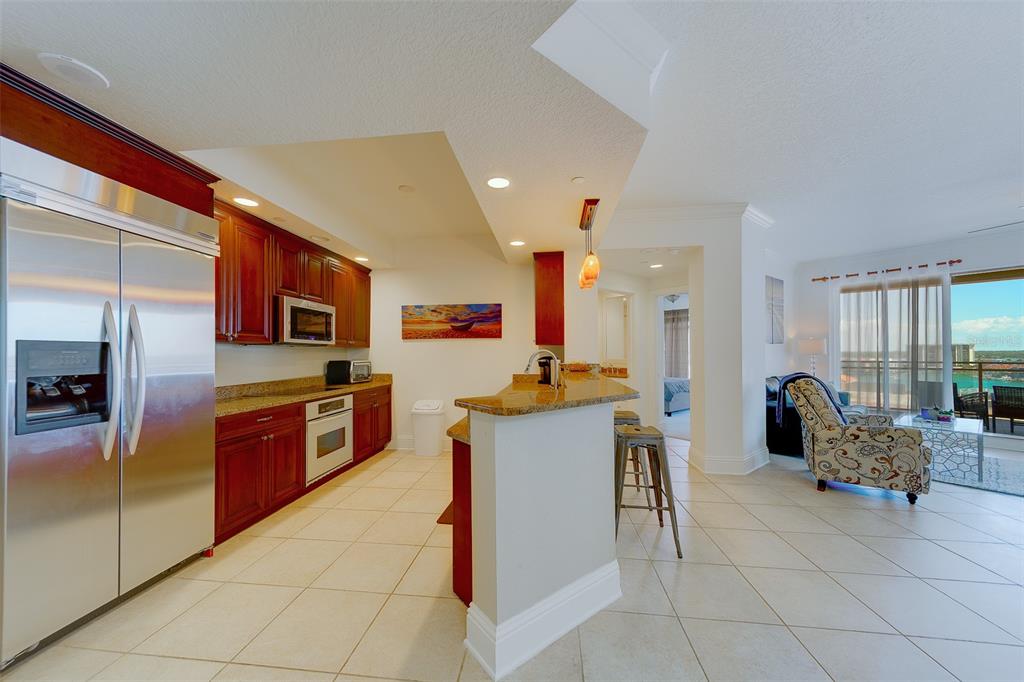 A kitchen with wood cabinets and granite countertops opens to a living area with balcony views — 11 BAYMONT STREET UNIT 1109, CLEARWATER BEACH, FL