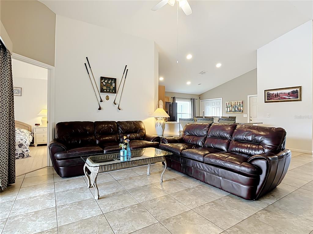 A living room with tile flooring, two dark leather sofas, and golf-themed wall decor — 604 CHADBURY WAY, KISSIMMEE, FL
