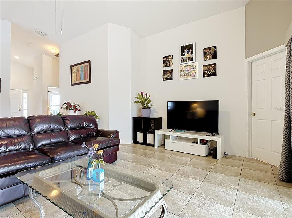 A living room features a dark leather sofa, a glass coffee table, and a television — 604 CHADBURY WAY, KISSIMMEE, FL