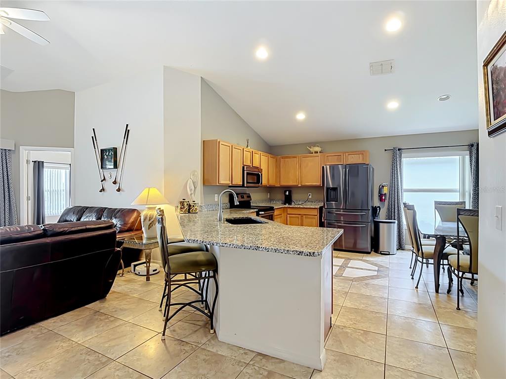 A kitchen with granite countertops, wooden cabinets, and a breakfast bar opens to a living area — 604 CHADBURY WAY, KISSIMMEE, FL