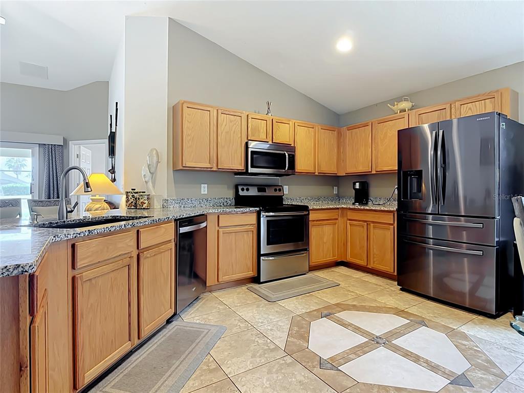A kitchen features light wood cabinets, granite countertops, stainless steel appliances, and tiled flooring — 604 CHADBURY WAY, KISSIMMEE, FL