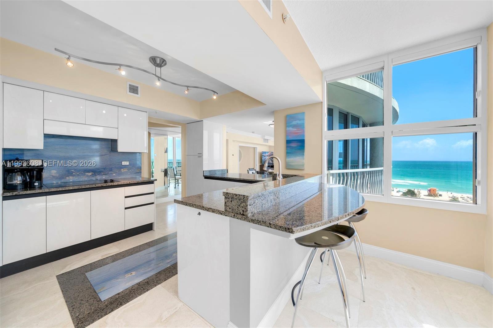 A modern kitchen features white cabinetry, granite countertops, a breakfast bar, and ocean views — 1500 Ocean Drive # 702, Miami Beach FL 33139, MIAMI BEACH, FL