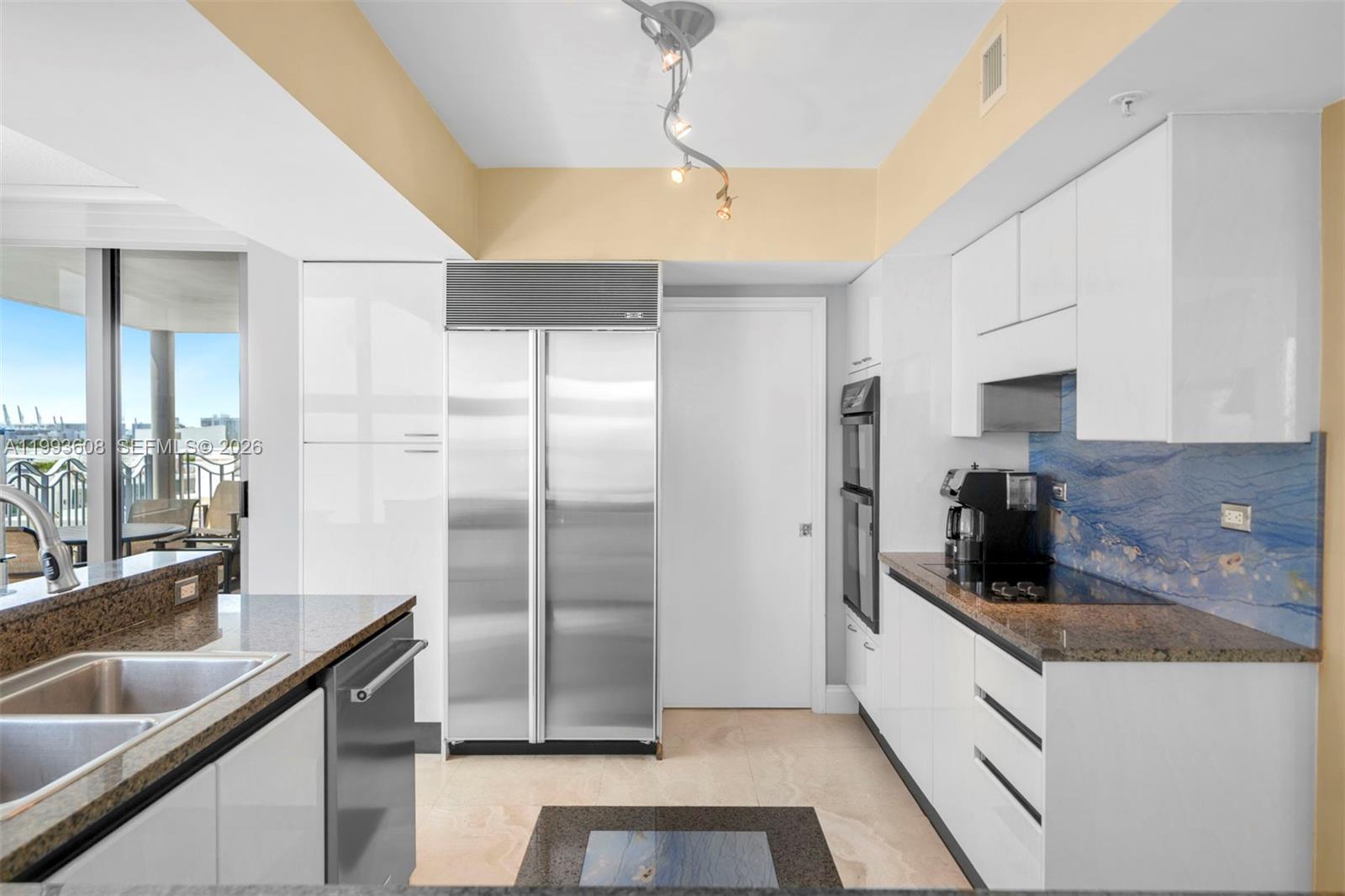 A modern kitchen features white cabinetry, stainless steel appliances, granite countertops, and a blue backsplash — 1500 Ocean Drive # 702, Miami Beach FL 33139, MIAMI BEACH, FL