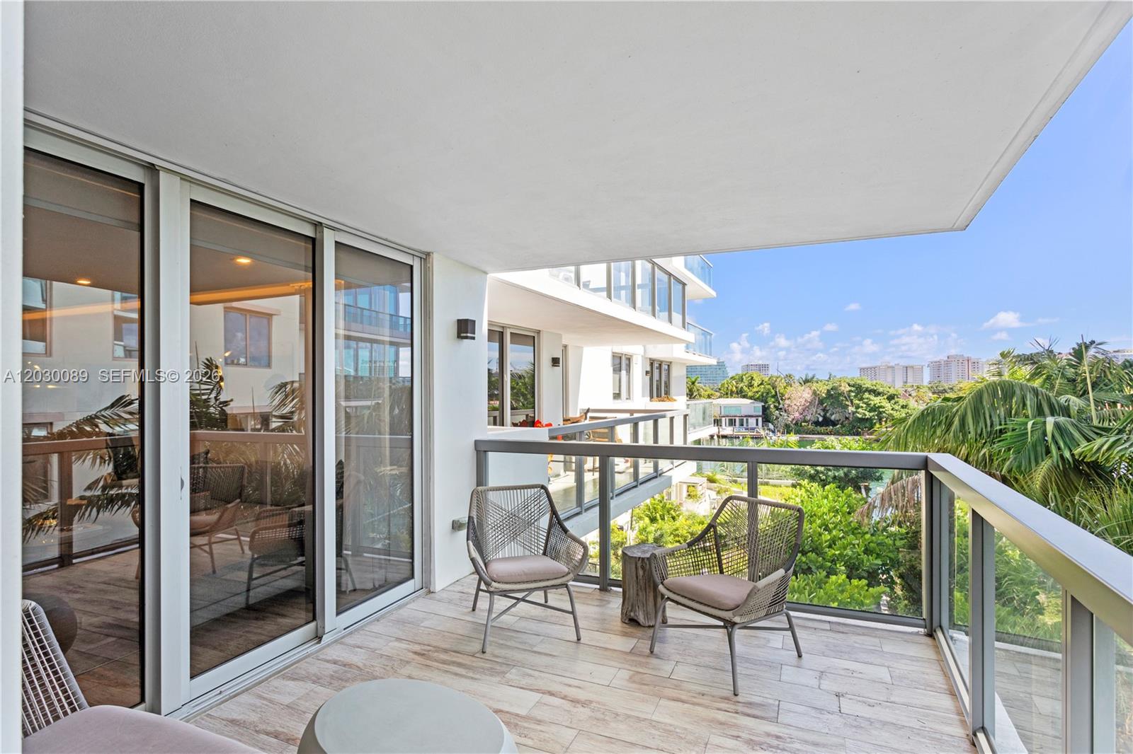 A balcony with tiled flooring, two chairs, and a glass railing overlooks trees and buildings — 9261 E Bay Harbor Dr # 407, Bay Harbor Islands FL 33154, BAY HARBOR ISLANDS, FL