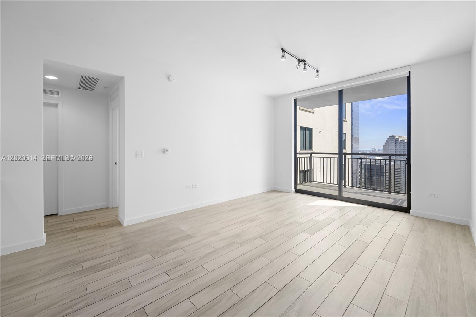 A bright, empty room features light wood-look tile flooring, white walls, and a sliding glass balcony door — 999 SW 1st Ave # 2911, Miami FL 33130, MIAMI, FL