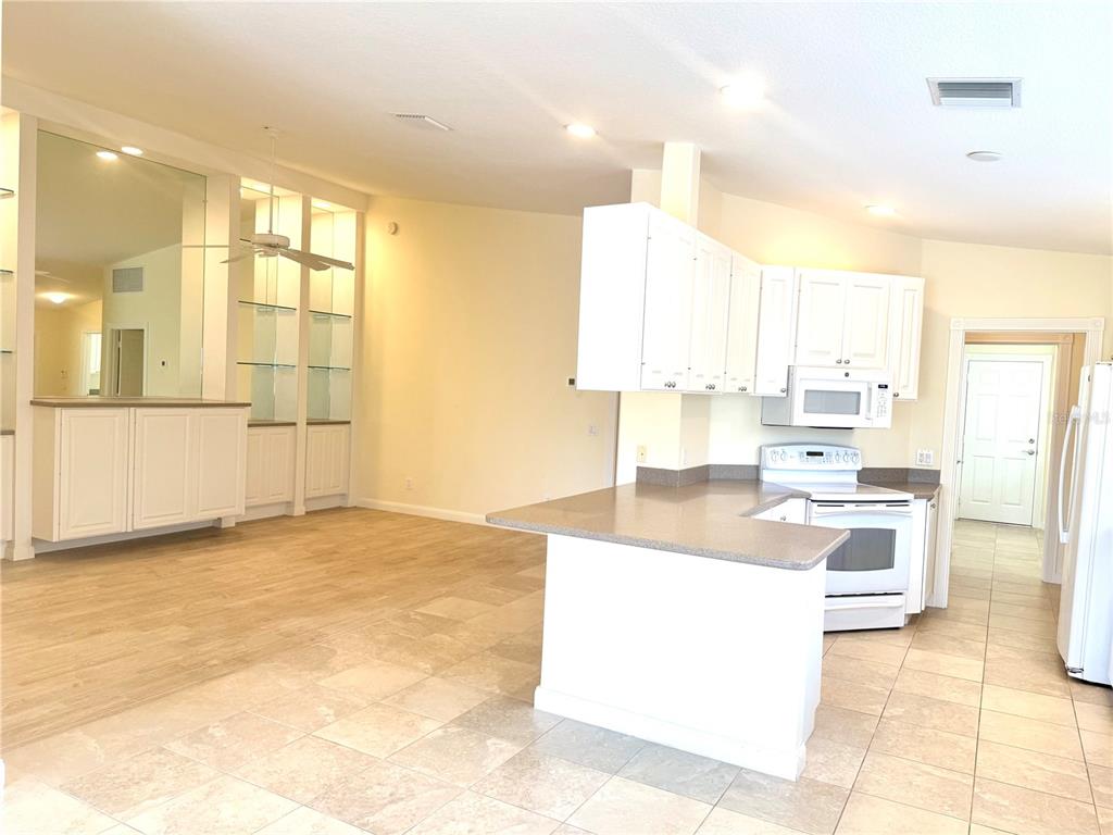 A kitchen with white cabinets and a breakfast bar opens into a living area — 6214 ERICE STREET, VENICE, FL