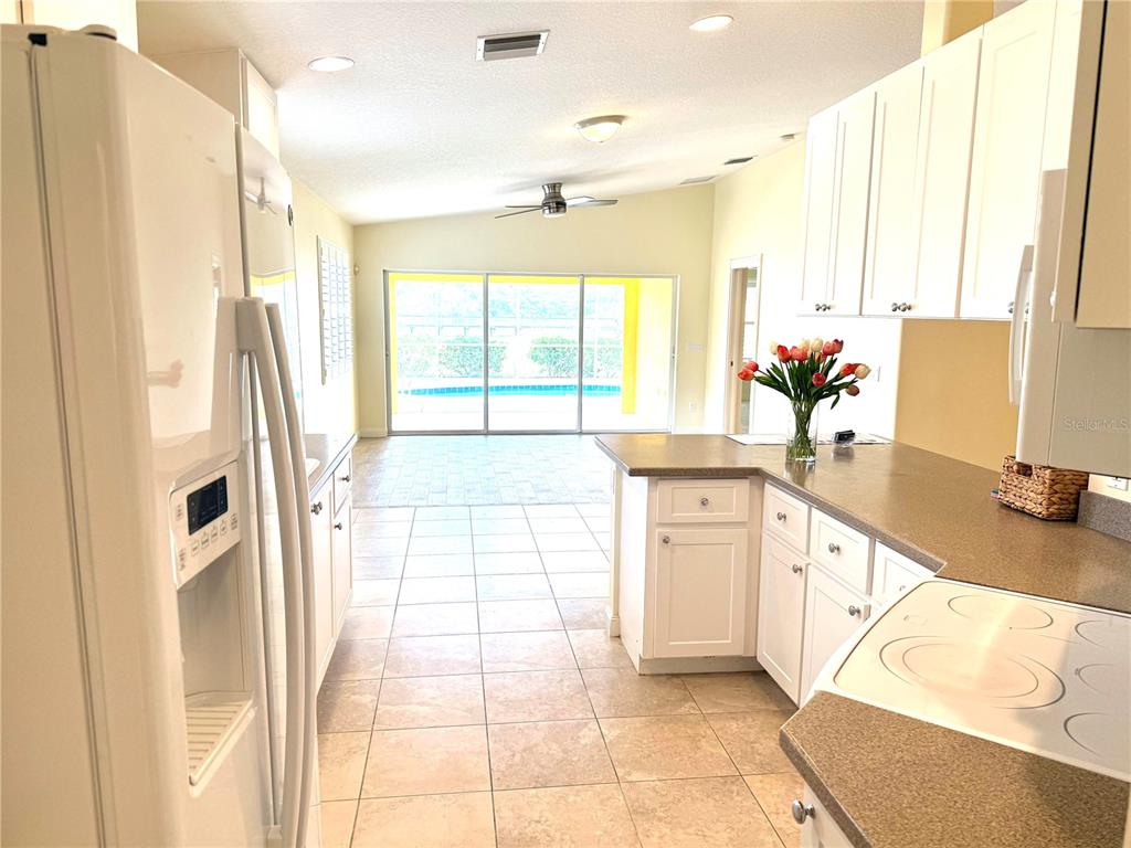 A kitchen with white cabinets and a view of a pool through sliding glass doors — 6214 ERICE STREET, VENICE, FL