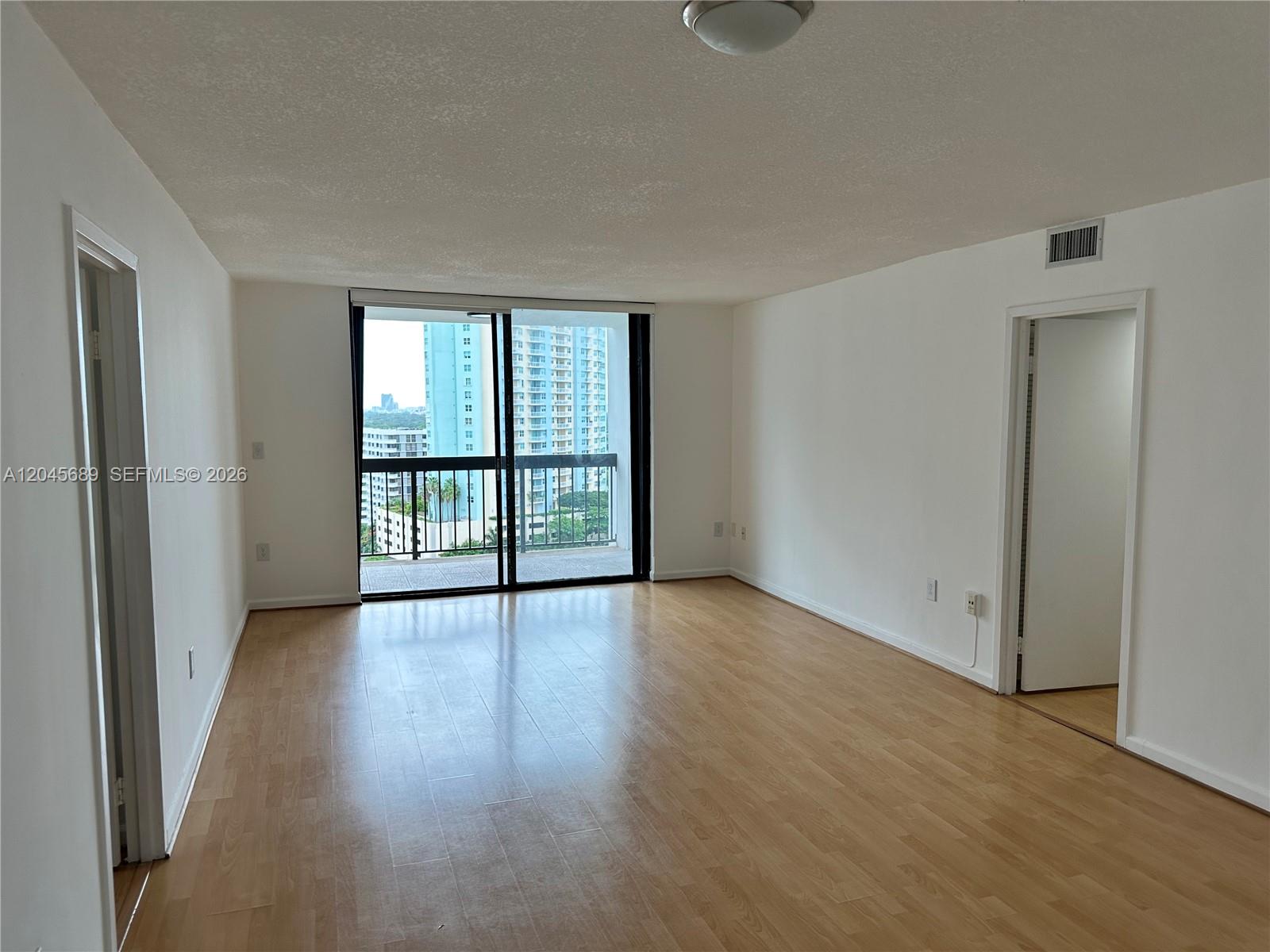 An empty living room with light wood flooring, white walls, and a sliding glass balcony door — 2333 Brickell Ave # 1610, Miami FL 33129, MIAMI, FL