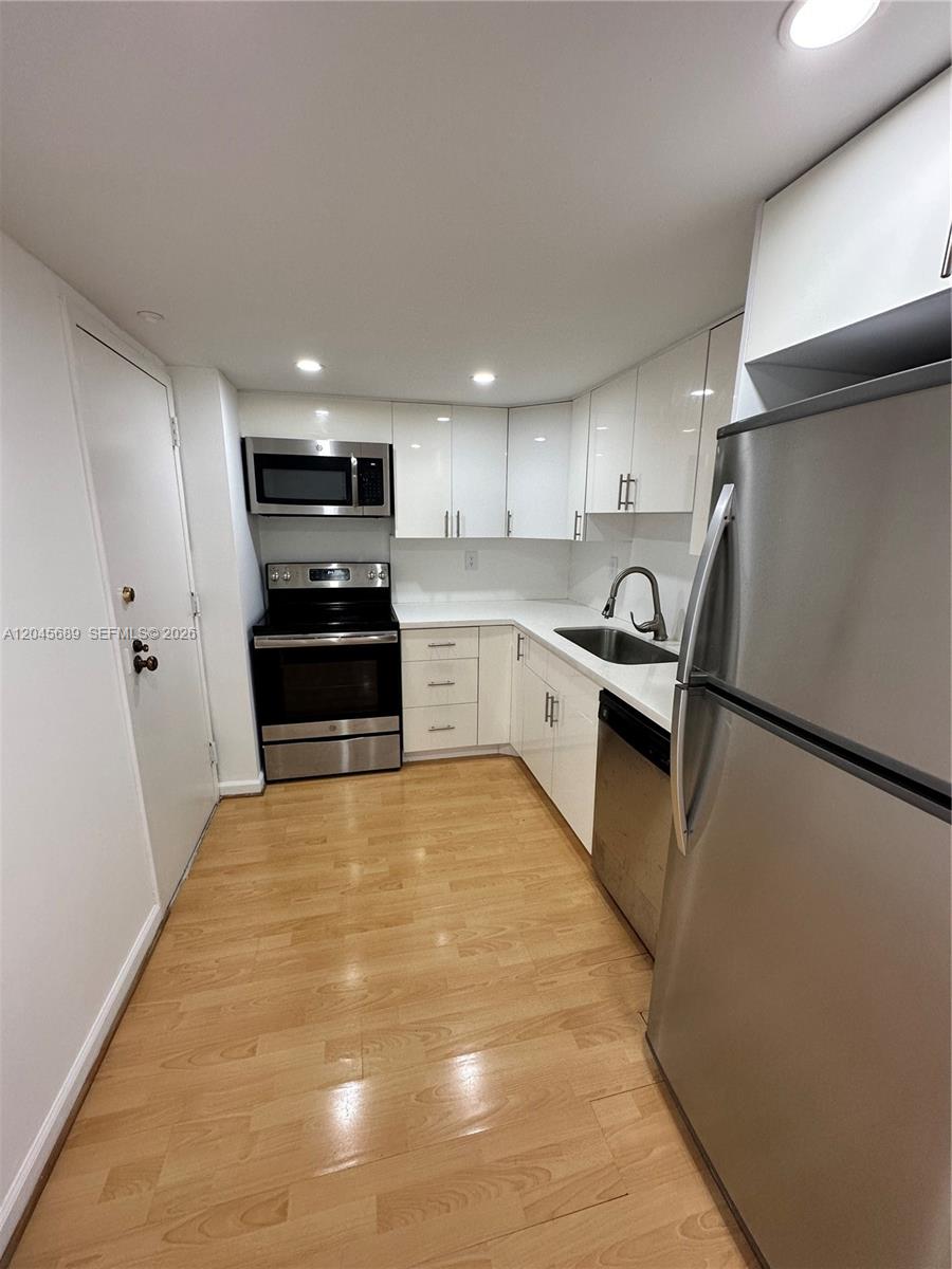 A galley kitchen features stainless steel appliances, white cabinetry, and light wood flooring — 2333 Brickell Ave # 1610, Miami FL 33129, MIAMI, FL