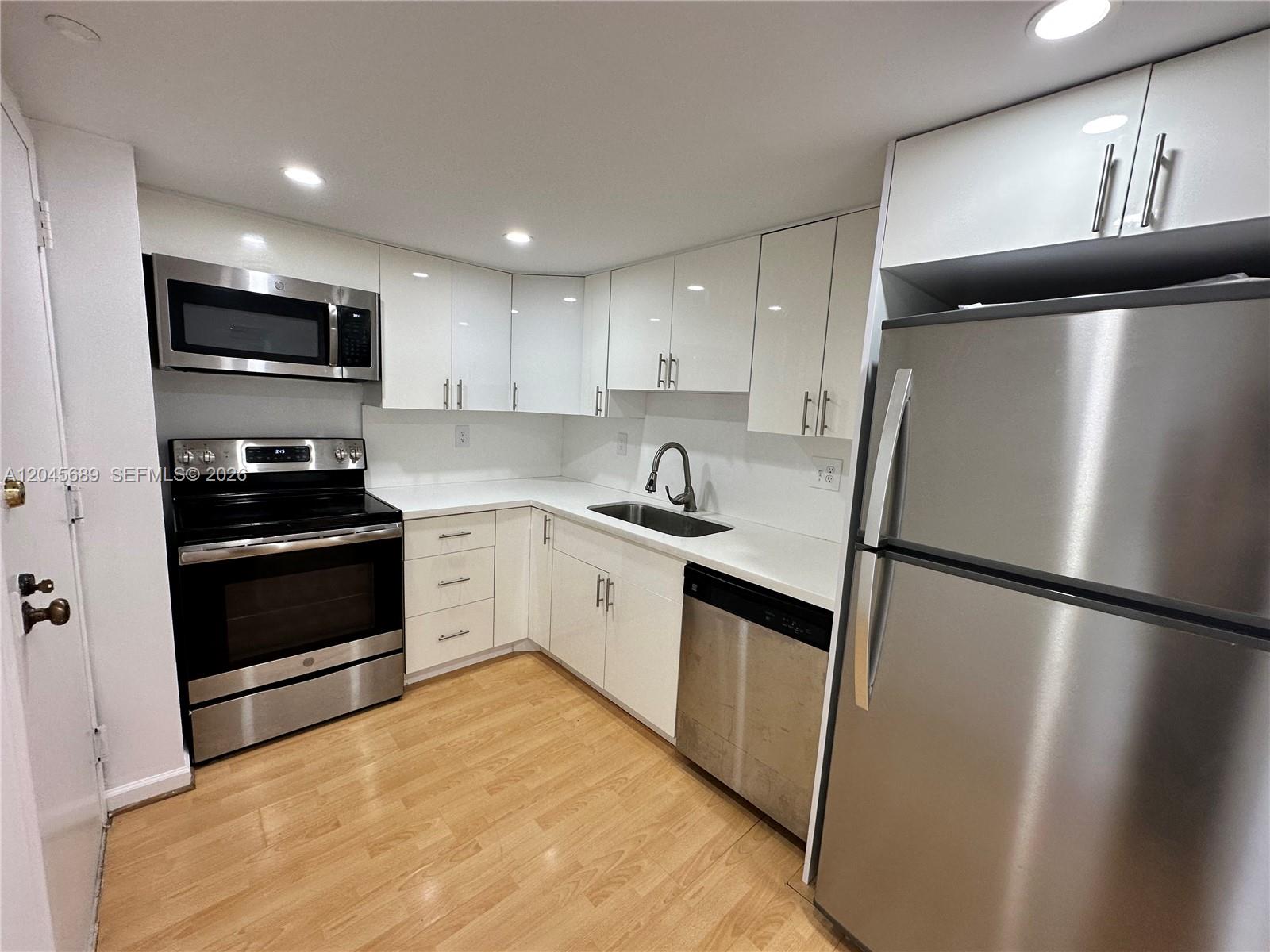 An empty living room features light wood-look flooring, beige walls, and a large white-framed sliding door — 2333 Brickell Ave # 1610, Miami FL 33129, MIAMI, FL