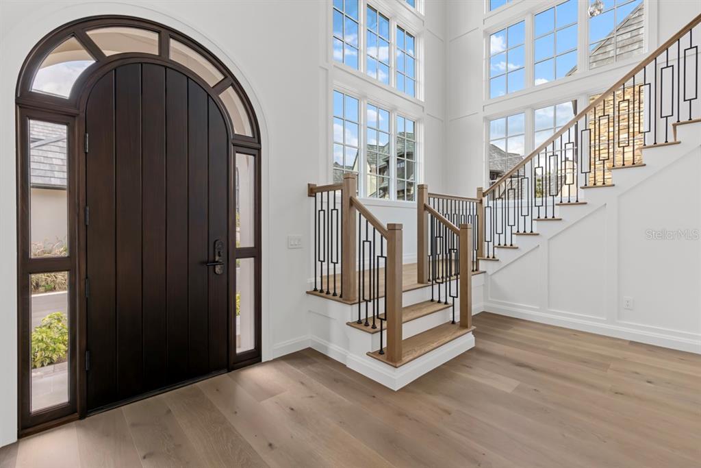 An entryway features a dark arched door, light wood floors, and a staircase with railings — 10335 WINTER SPARKLE CIRCLE, GOLDEN OAK, FL