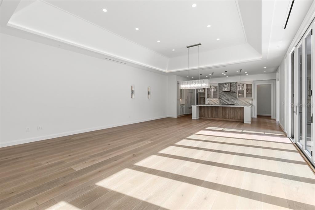 A spacious, modern open-concept living area with light wood floors, a tray ceiling, and kitchen — 10335 WINTER SPARKLE CIRCLE, GOLDEN OAK, FL