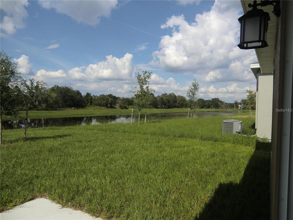 A grassy backyard overlooks a pond with trees under a cloudy blue sky — 780 DARING DRIVE, DAVENPORT, FL