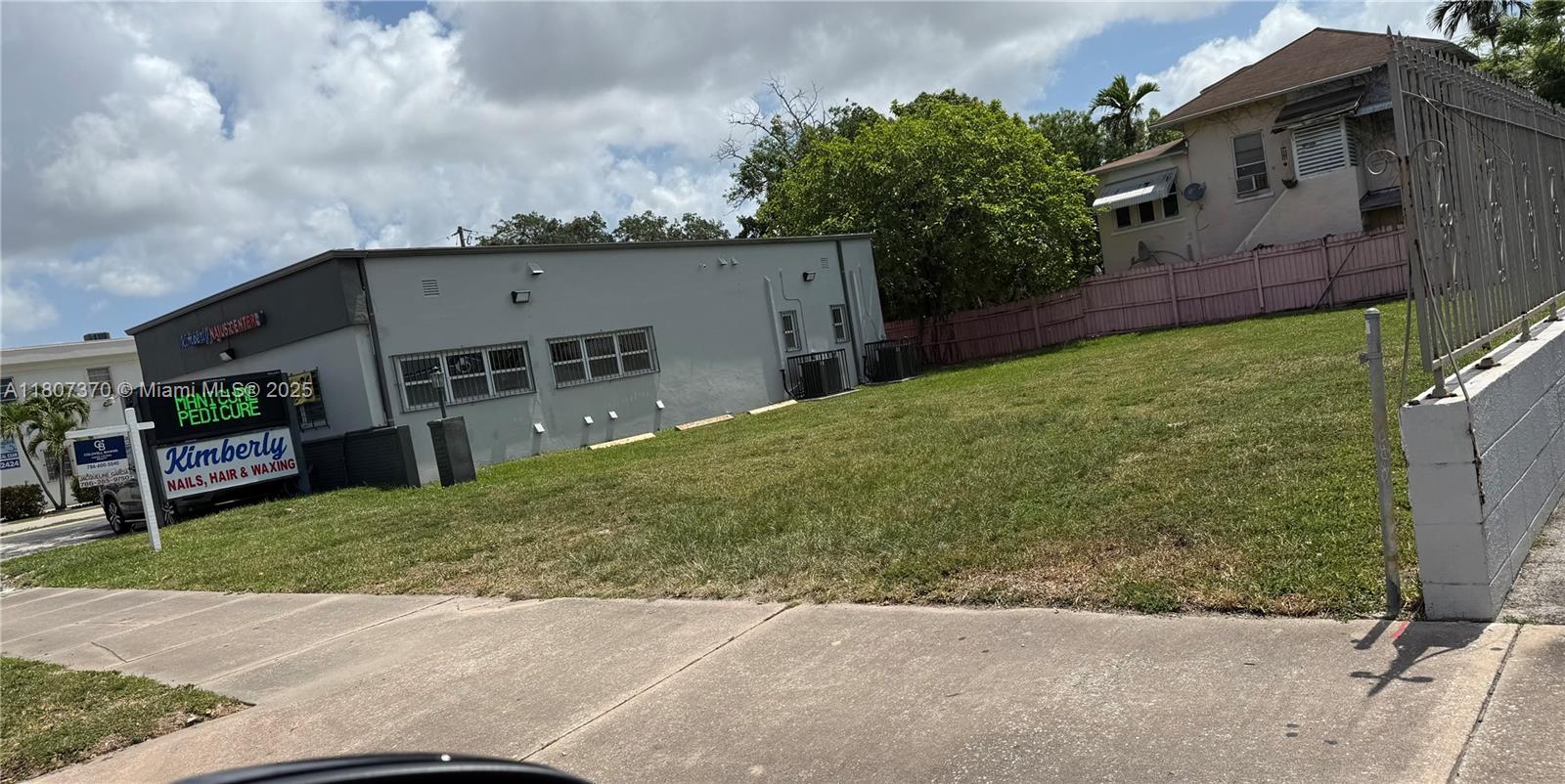 A gray commercial building sits next to an empty, grass-covered lot under a cloudy sky — 1959 SW 27th Ave, Miami FL 33145, MIAMI, FL