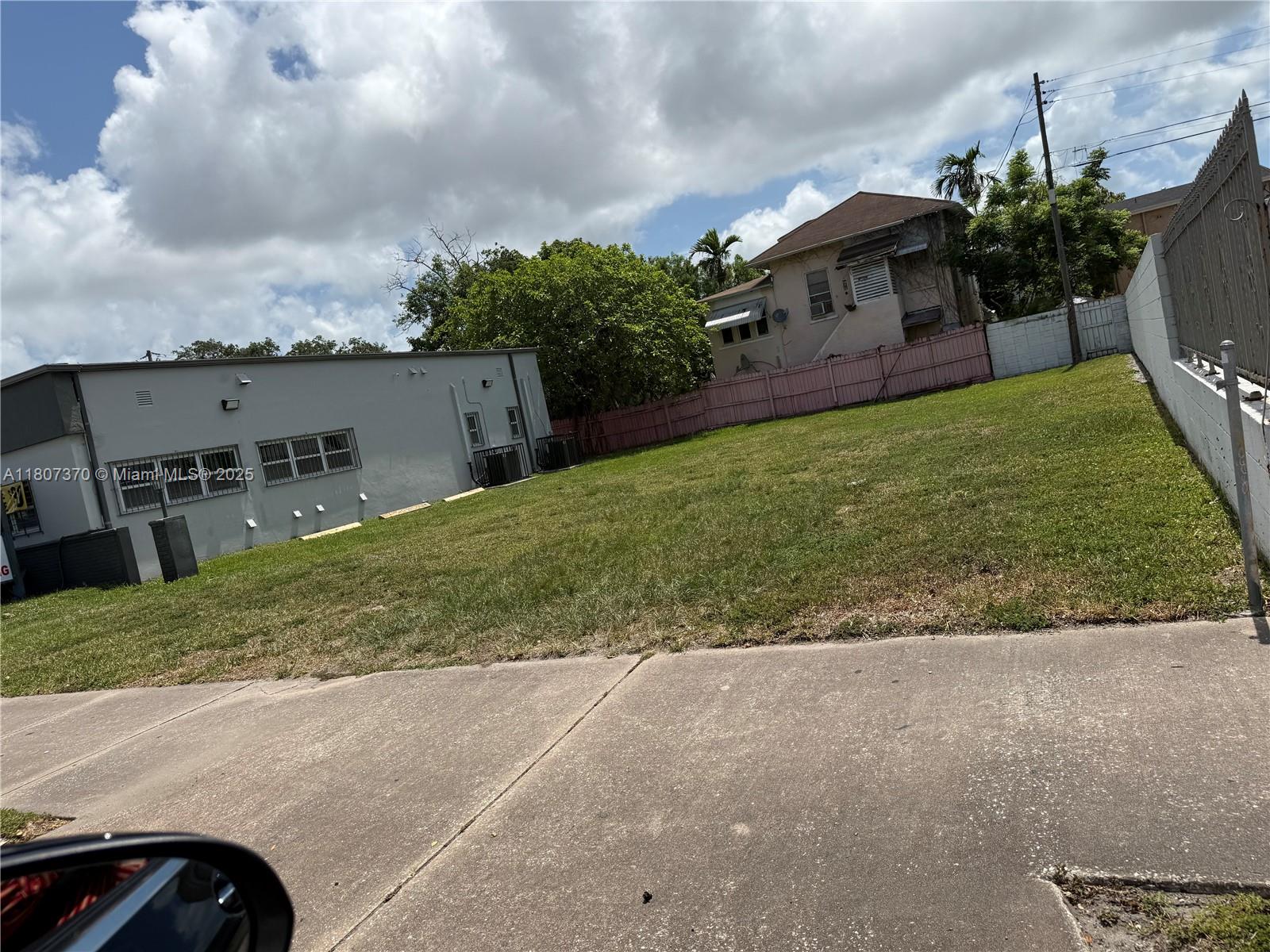 A grassy vacant lot sits between a gray building and a fenced residential property — 1959 SW 27th Ave, Miami FL 33145, MIAMI, FL