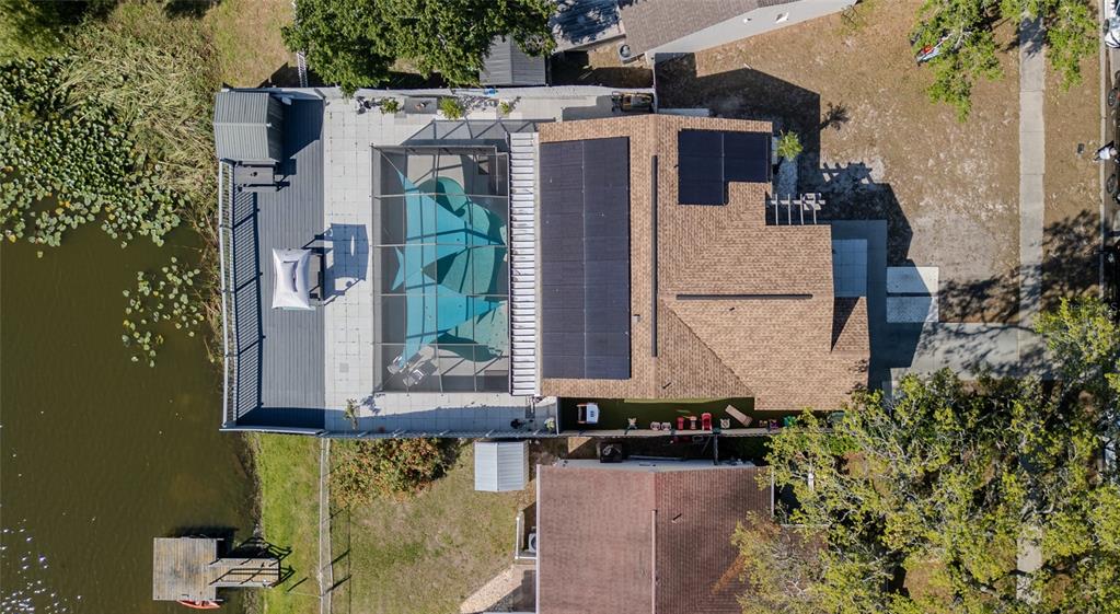 An aerial view shows a house with a pool enclosure, solar panels, and a wooden dock — 12416 QUEENSLAND LANE, TAMPA, FL