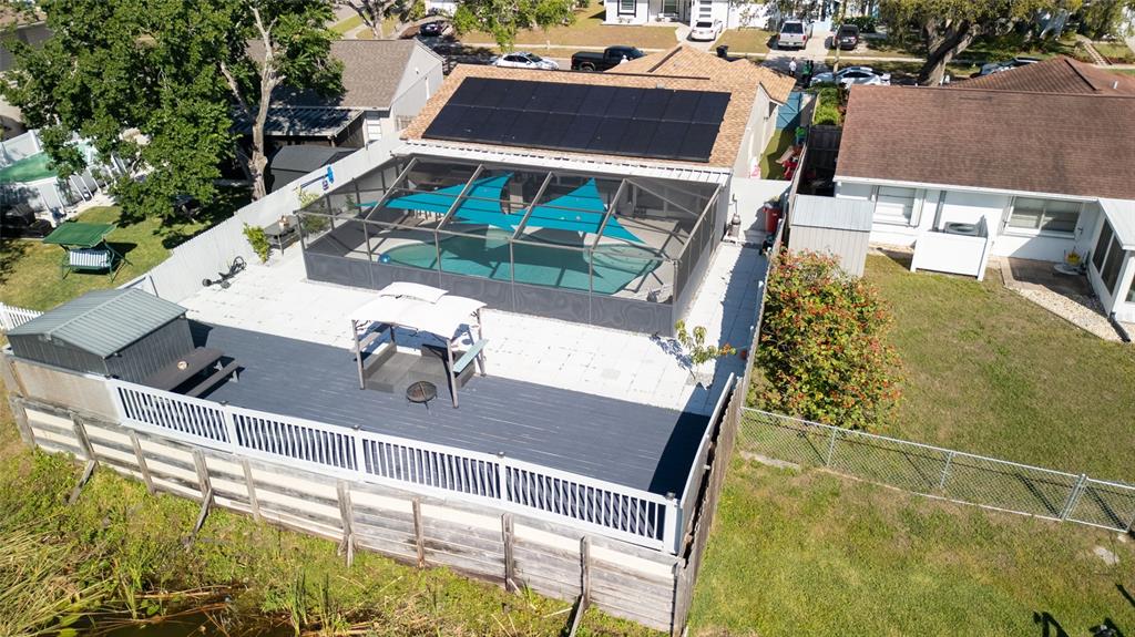 An aerial view shows a house with solar panels, a screened pool, and a wooden deck — 12416 QUEENSLAND LANE, TAMPA, FL