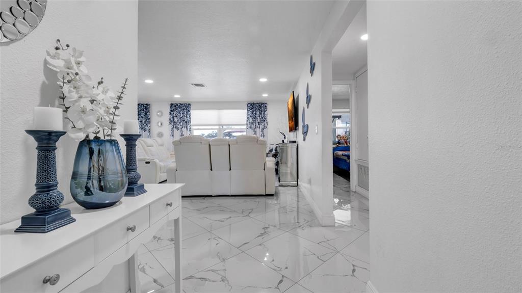 A white console table with blue decor sits in a hallway leading to a living room — 12416 QUEENSLAND LANE, TAMPA, FL