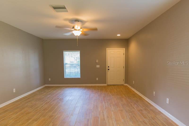 An empty room features light-colored wood-look tile flooring, gray walls, a ceiling fan, and a door — 5879 FISHHAWK RIDGE DRIVE, LITHIA, FL