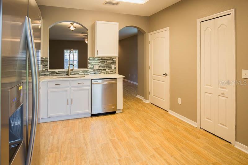 A kitchen with white cabinets, stainless steel appliances, a tiled backsplash, and light wood flooring — 5879 FISHHAWK RIDGE DRIVE, LITHIA, FL