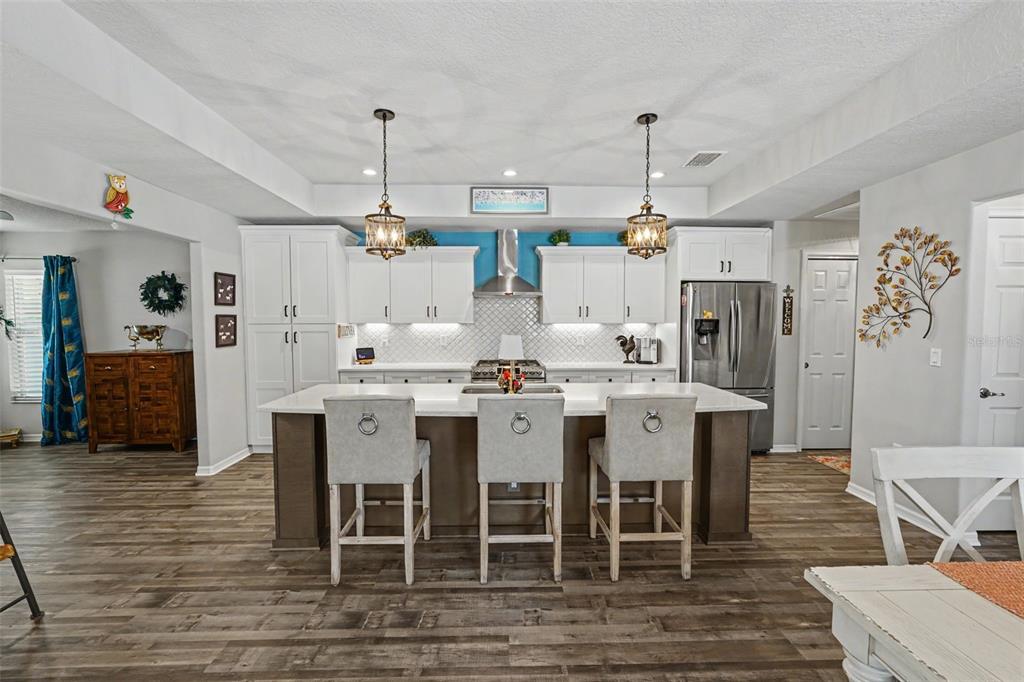 A kitchen features a central island with three chairs, white cabinets, and wood-look flooring — 13416 WHITMARSH STREET, SPRING HILL, FL