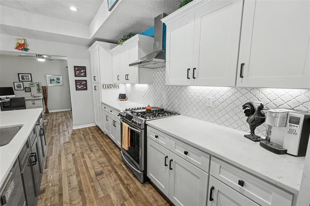 A kitchen features white cabinets, a patterned tile backsplash, stainless steel appliances, and wood flooring — 13416 WHITMARSH STREET, SPRING HILL, FL