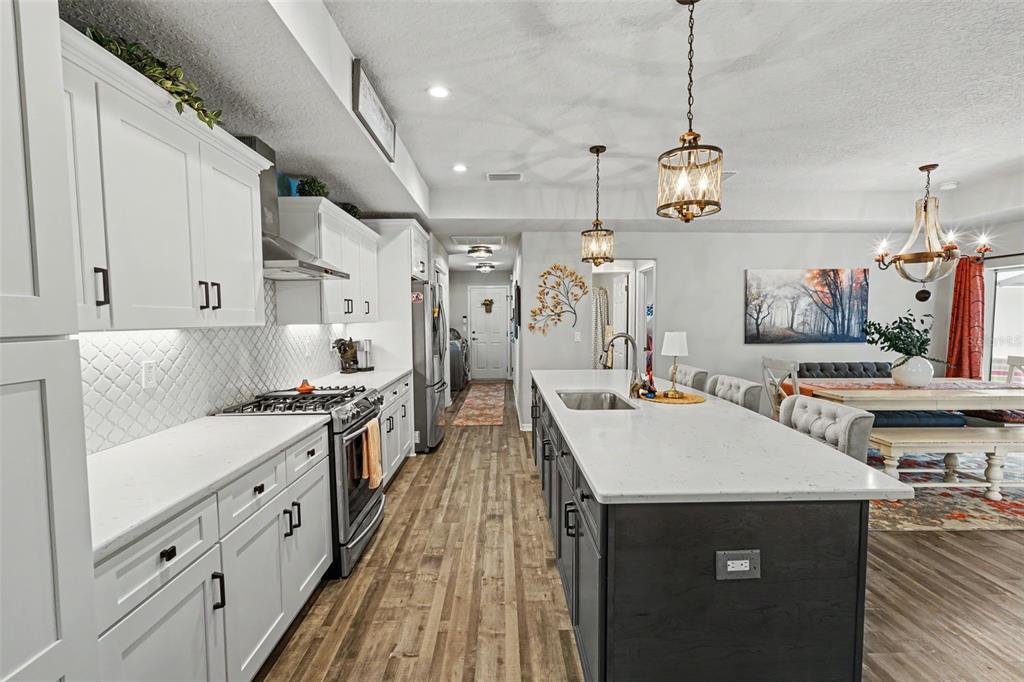 A kitchen features white cabinets, a dark island with a sink, and wood-look flooring — 13416 WHITMARSH STREET, SPRING HILL, FL
