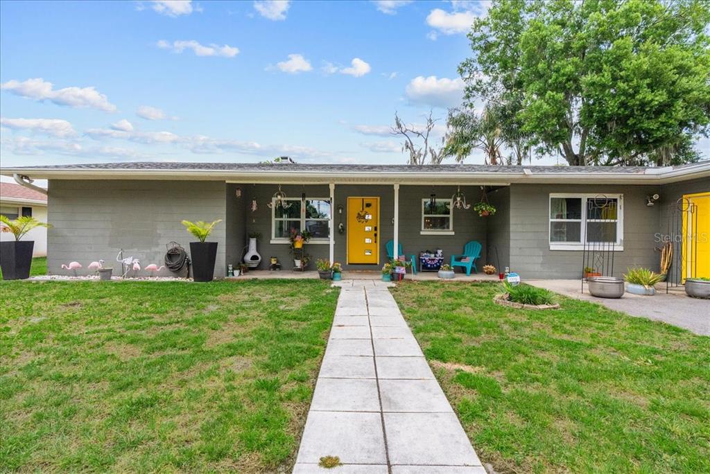 A single-story gray house features a bright yellow front door and a concrete walkway — 4881 LAKE CECILE DR, KISSIMMEE, FL