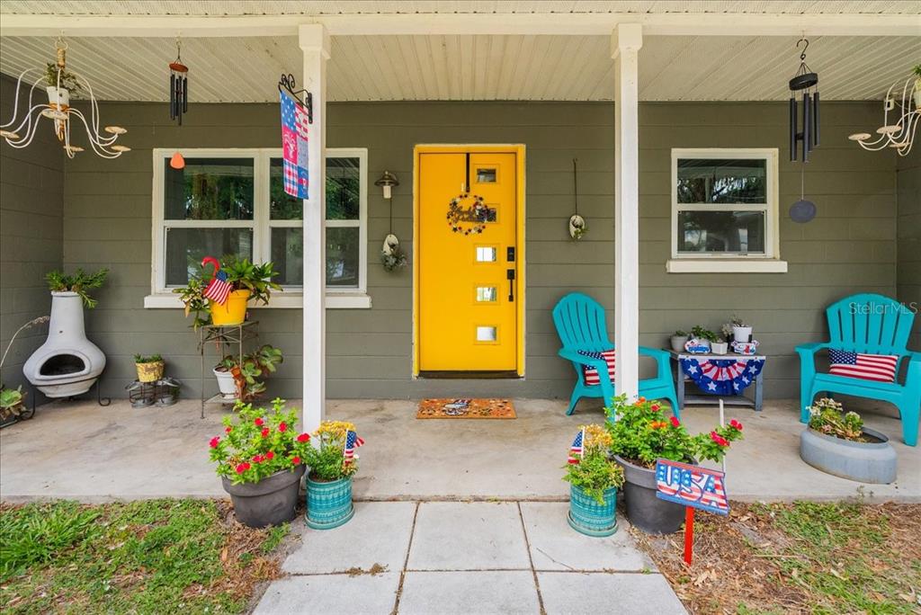 A front porch features a bright yellow door, two turquoise chairs, and potted plants — 4881 LAKE CECILE DR, KISSIMMEE, FL