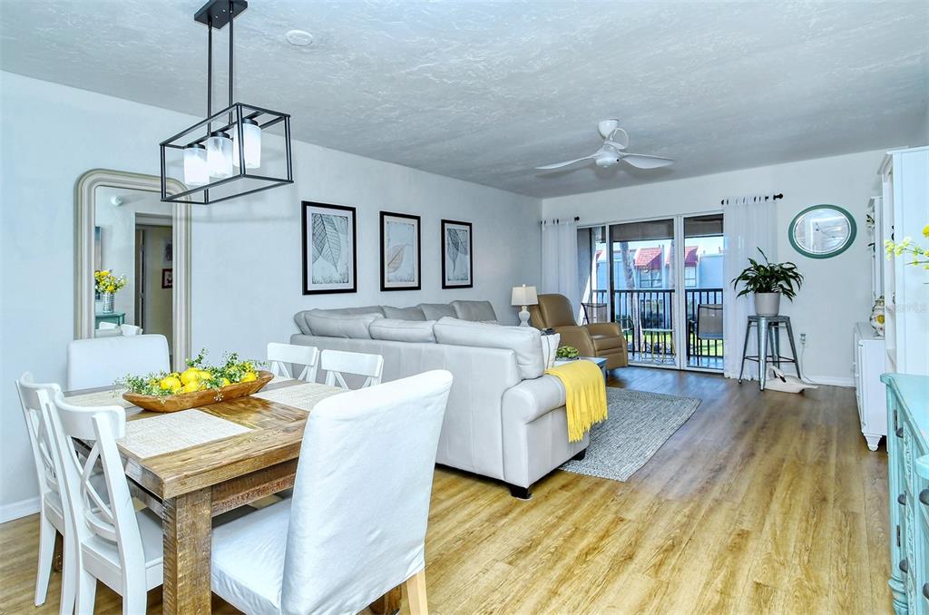 A dining area and living room feature light wood flooring, white furniture, and a balcony — 1801 GULF DRIVE N UNIT 275, BRADENTON BEACH, FL