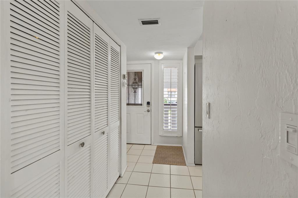 A hallway with white louvered closet doors, tiled flooring, and a white front door — 1801 GULF DRIVE N UNIT 275, BRADENTON BEACH, FL