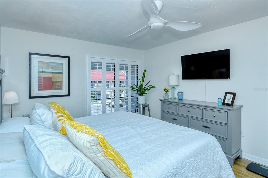 A bedroom features a bed with yellow pillows, a gray dresser, and a ceiling fan — 1801 GULF DRIVE N UNIT 275, BRADENTON BEACH, FL