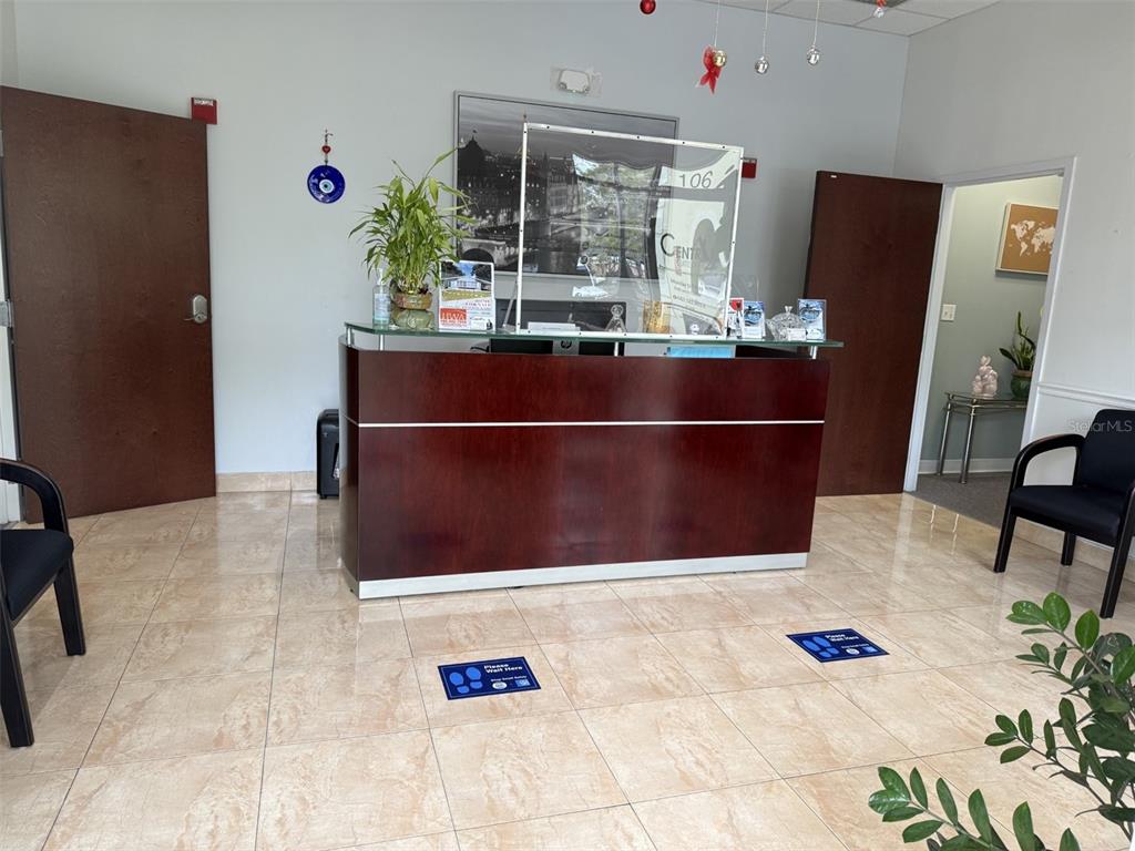 A reception area features a dark wood desk, tile flooring, and two chairs for visitors — 12250 MENTA STREET UNIT 106, ORLANDO, FL