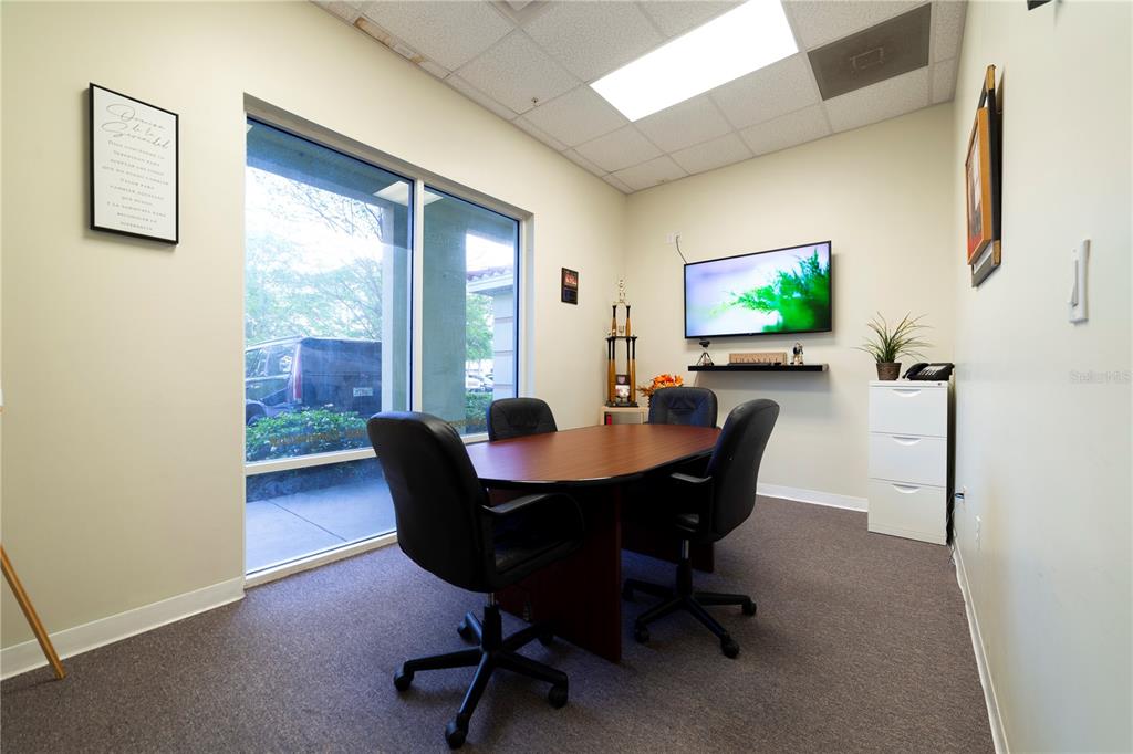 A small office features a conference table, four chairs, a wall-mounted television, and a window — 12250 MENTA STREET UNIT 106, ORLANDO, FL