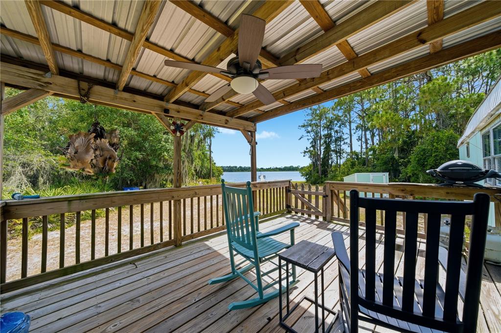 A covered wooden deck features a ceiling fan, rocking chairs, and a view of a lake — 3144 HOLIDAY BEACH DRIVE, AVON PARK, FL