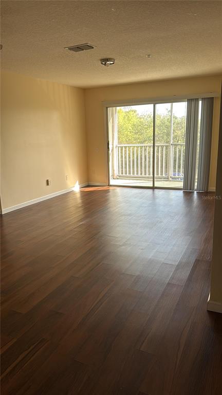 An empty living room features dark wood-look flooring, light-colored walls, and a sliding glass door — 3950 SOUTHPOINTE DRIVE UNIT 418, ORLANDO, FL