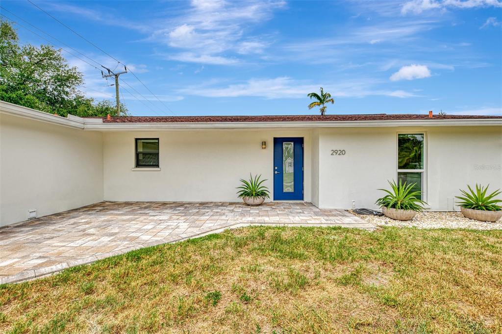 A single-story house exterior features a blue front door, paved patio, and white walls — 2920 GULF GATE DRIVE, SARASOTA, FL