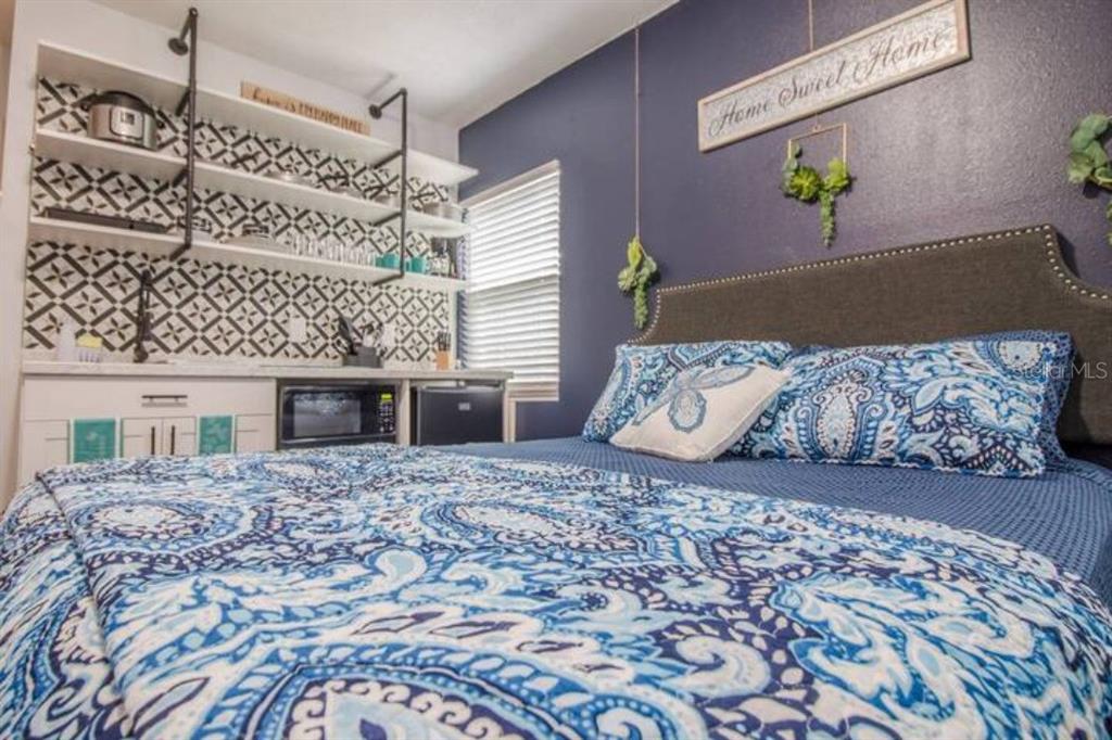 A bedroom with a blue accent wall, patterned bedding, and a kitchenette with open shelving — 2014 NEWMAN ST UNIT 3, ORLANDO, FL