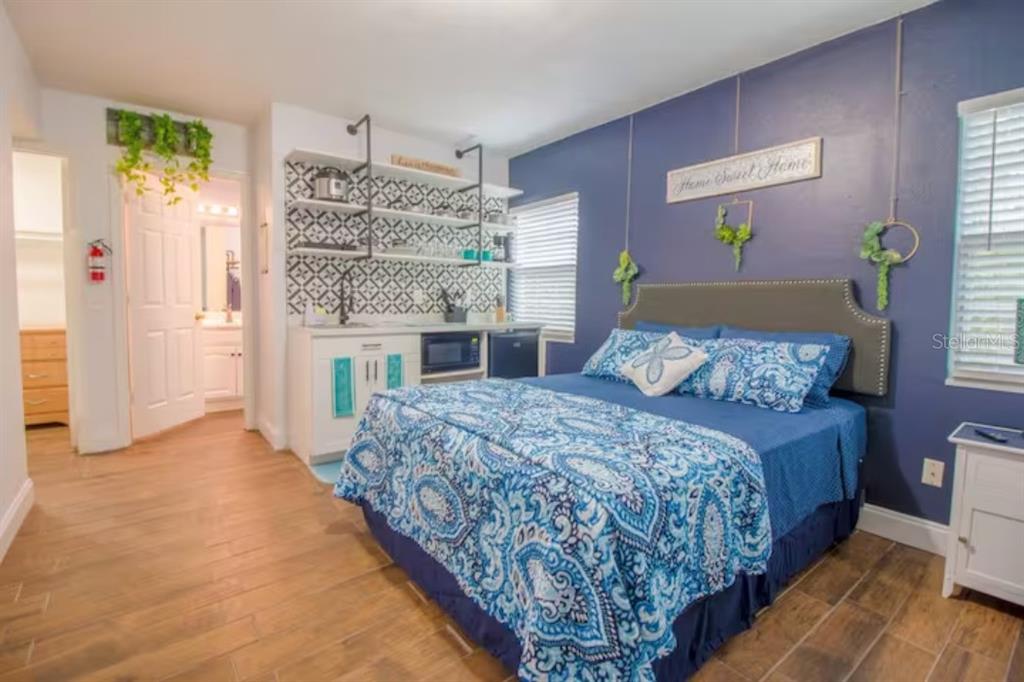 A bedroom with a blue accent wall, a patterned bedspread, and a small kitchenette area — 2014 NEWMAN ST UNIT 3, ORLANDO, FL