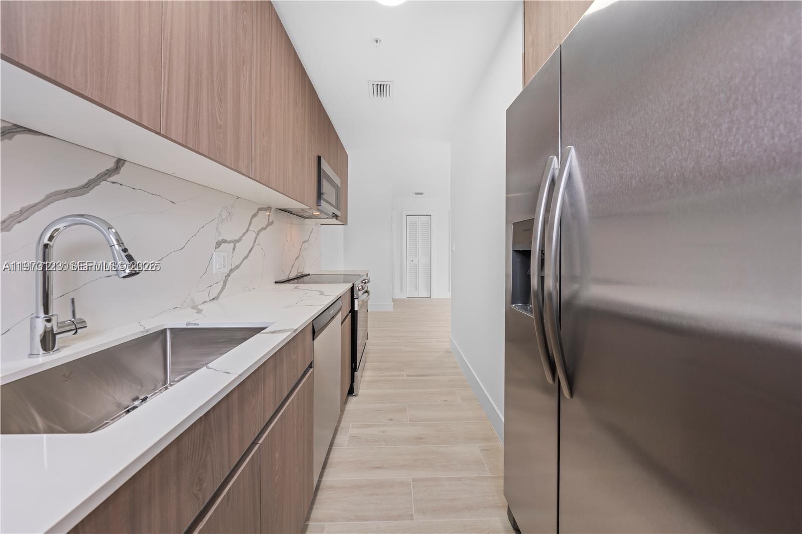 A galley kitchen features wood-tone cabinets, stainless steel appliances, and white marble-patterned countertops — 32 NW 14th Ave # 3, Miami FL 33125, MIAMI, FL