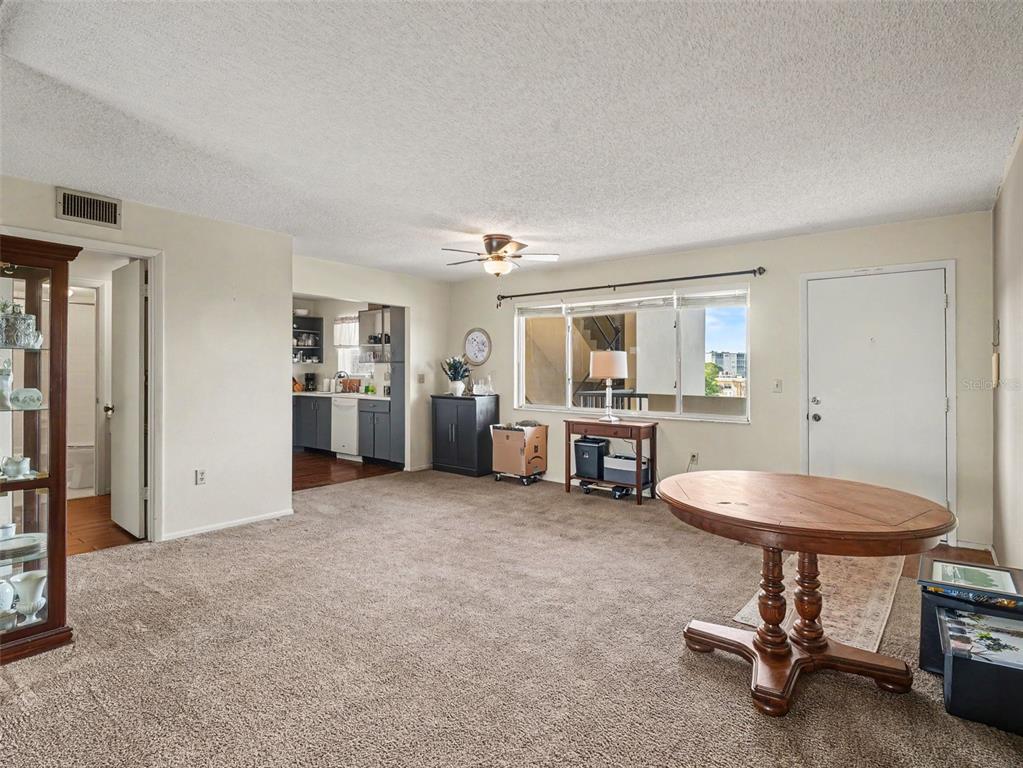 A carpeted living room features a round wooden table, a ceiling fan, and an adjacent kitchen — 4460 IRONWOOD CIRCLE UNIT 402AD, BRADENTON, FL