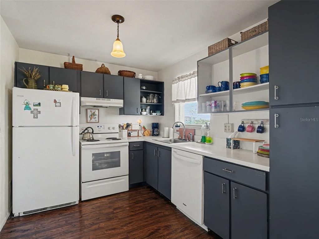 A kitchen features dark grey cabinets, white appliances, open shelving, and dark wood-look flooring — 4460 IRONWOOD CIRCLE UNIT 402AD, BRADENTON, FL