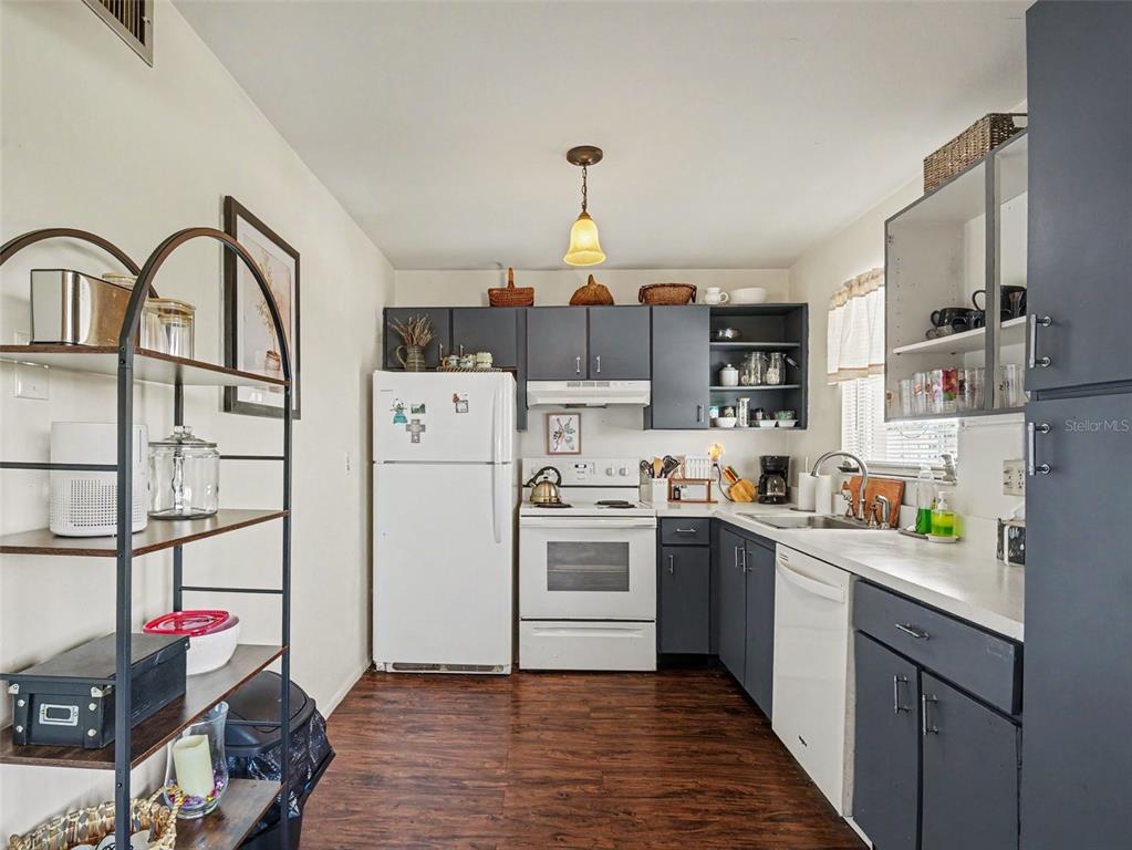 A kitchen features dark gray cabinets, white appliances, wood-look flooring, and an open metal shelving unit — 4460 IRONWOOD CIRCLE UNIT 402AD, BRADENTON, FL
