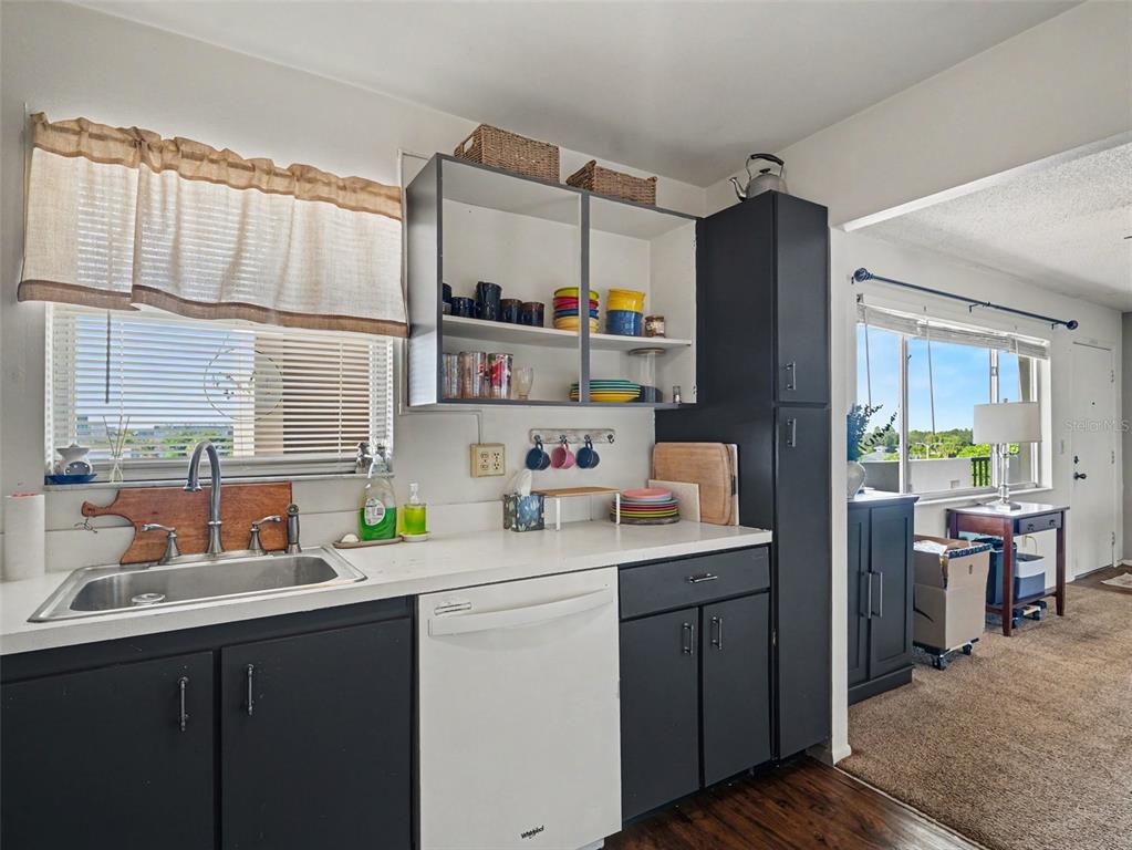 A kitchen features dark cabinets, a white dishwasher, open shelving, and a stainless steel sink — 4460 IRONWOOD CIRCLE UNIT 402AD, BRADENTON, FL