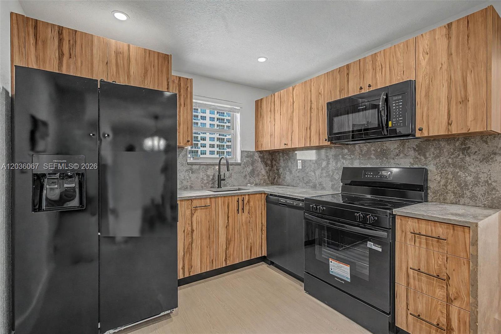 A kitchen features wood-grain cabinets, black appliances, and a gray stone-look backsplash — 5555 Collins Ave # 7B, Miami Beach FL 33140, MIAMI BEACH, FL