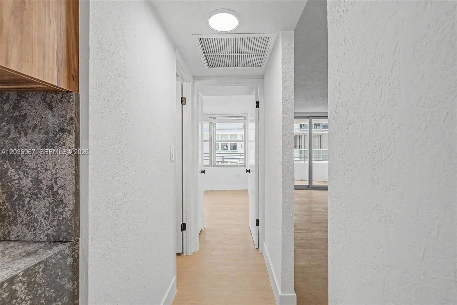 A hallway with white walls and light wood flooring leads to an open living area — 5555 Collins Ave # 7B, Miami Beach FL 33140, MIAMI BEACH, FL