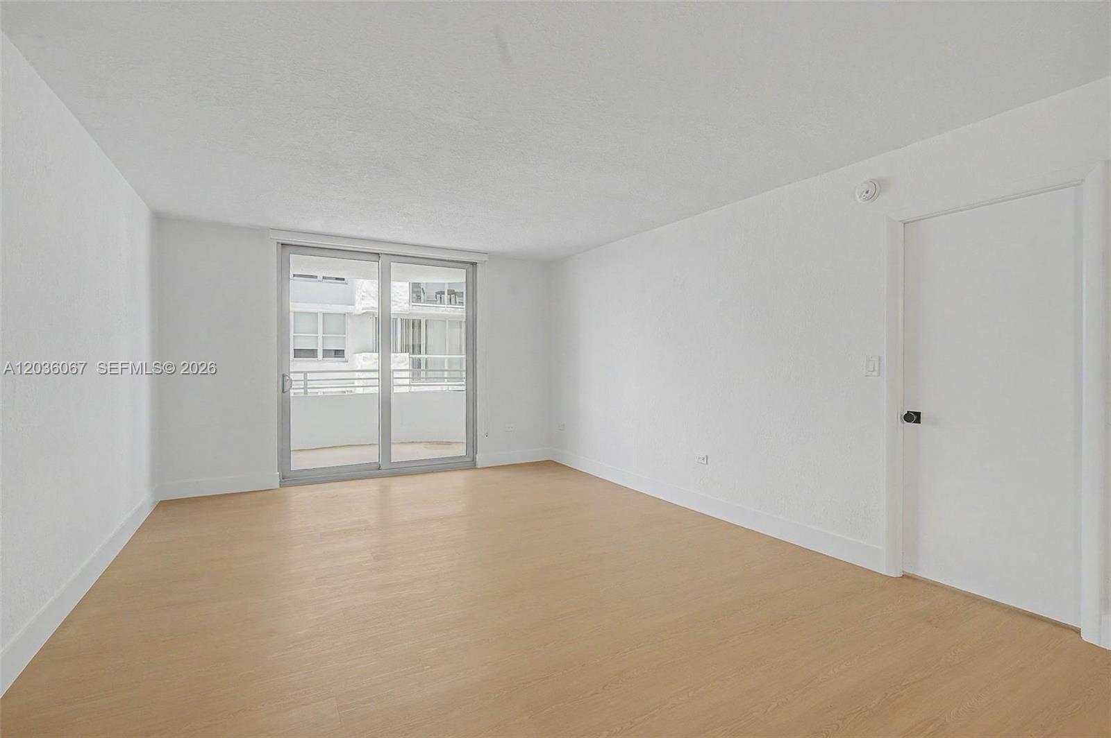 An empty room features light wood-look flooring, white walls, and a sliding glass balcony door — 5555 Collins Ave # 7B, Miami Beach FL 33140, MIAMI BEACH, FL