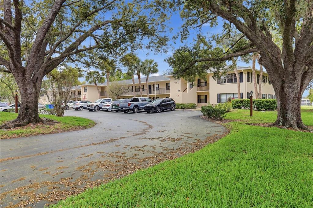 A multi-story apartment building with a parking lot surrounded by large trees and grass — 7130 FAIRWAY BEND LANE UNIT 291, SARASOTA, FL